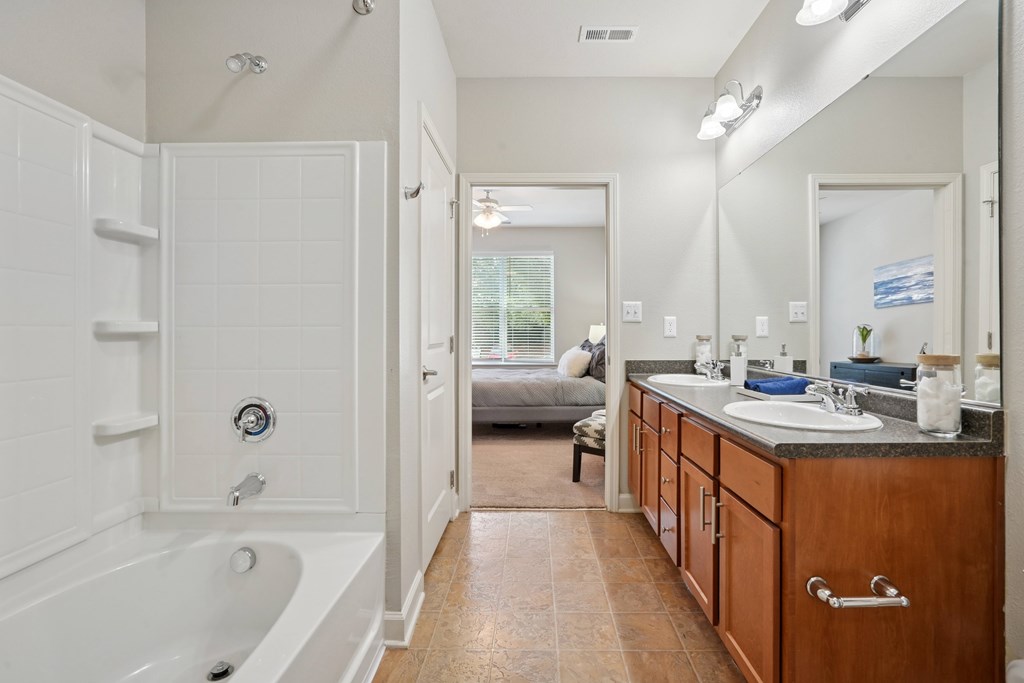 A bathroom with a white tub and wooden cabinets.