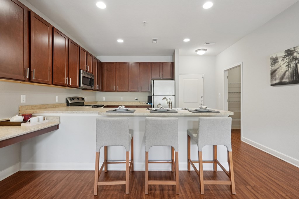 A kitchen with a white counter and brown chairs.
