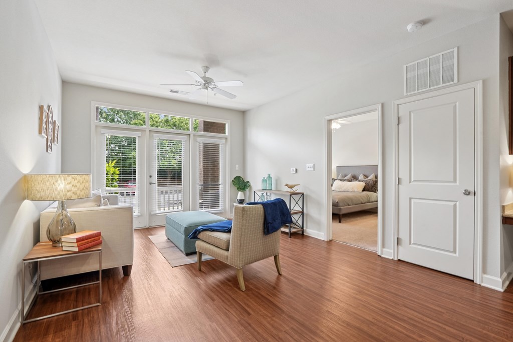 A living room with a sofa, a chair, a table, a fan, and a window with a view of the outdoors.