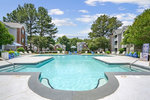 A large swimming pool in a residential area with trees and houses in the background.