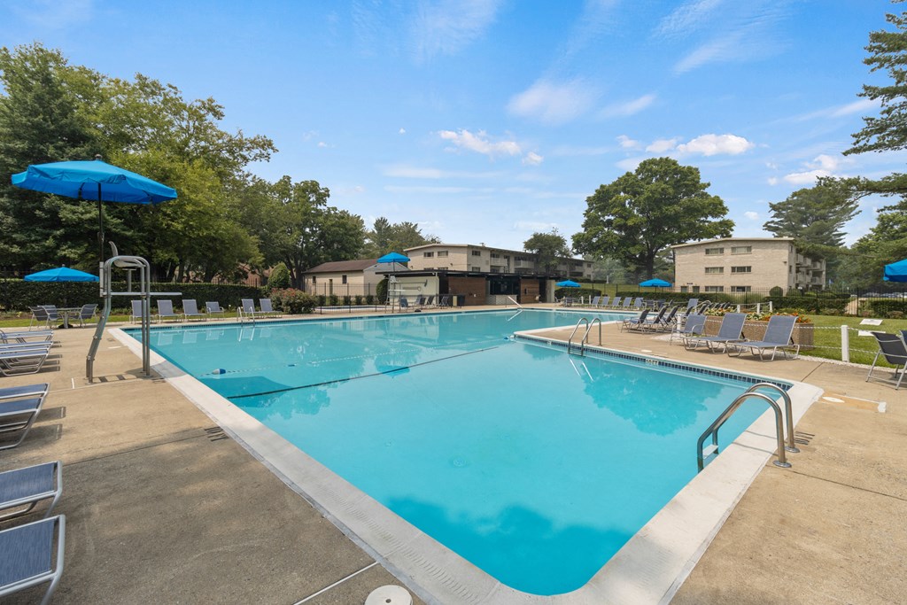 a swimming pool with chairs and umbrellas and buildings in the background