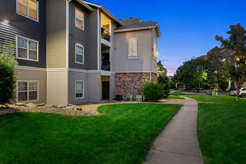 a sidewalk in front of an apartment building with green grass