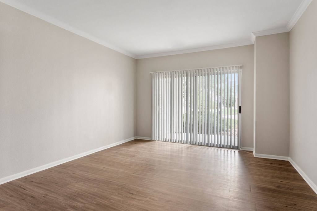 the living room of an apartment with wood flooring and a window with blinds