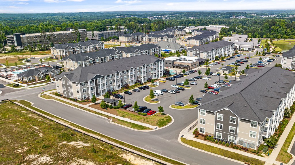 an aerial view of a large apartment complex with a parking lot and trees in the background
