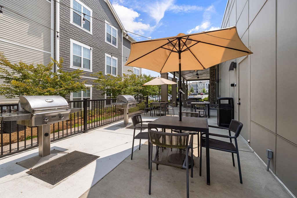 a patio with a table and chairs with an umbrella and a grill