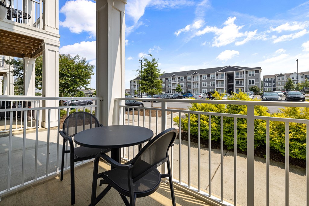 a patio with a table and two chairs on a balcony with a view of a parking lot