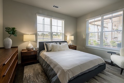 A bedroom with a large bed, a nightstand with a lamp, and a chair.