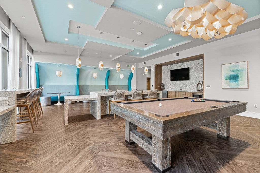 A pool table is in the middle of a room with a bar and chairs.