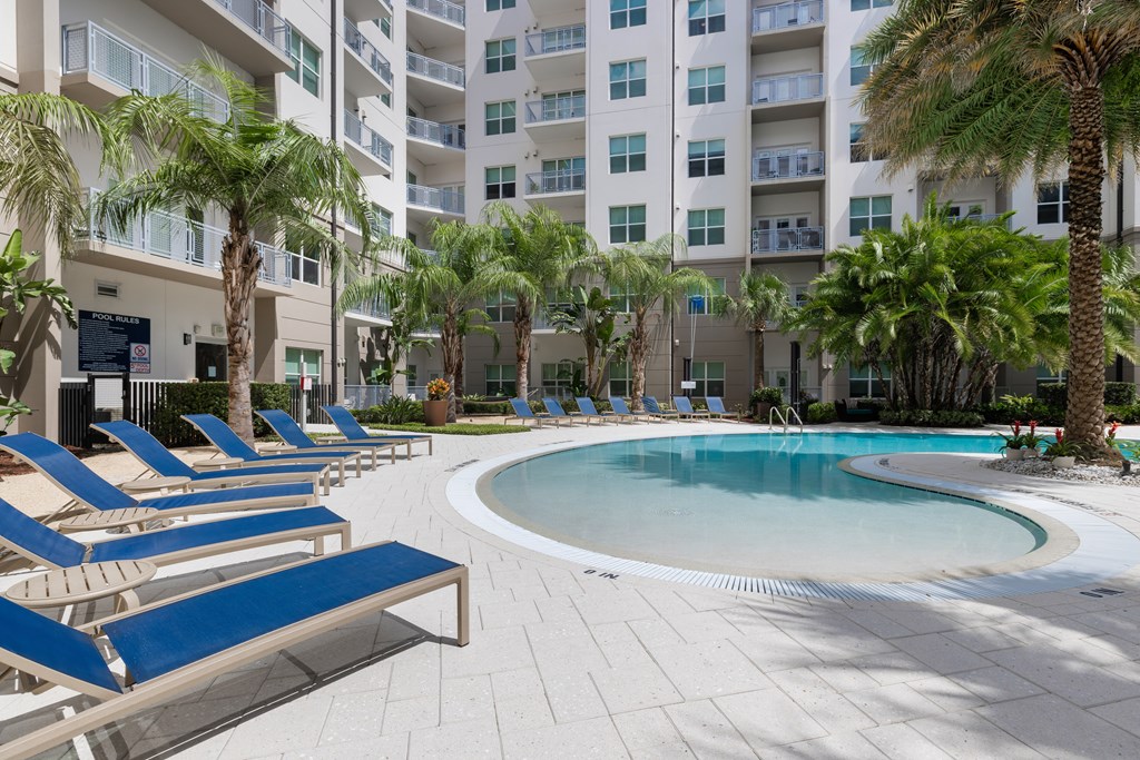A pool surrounded by palm trees and lounge chairs.