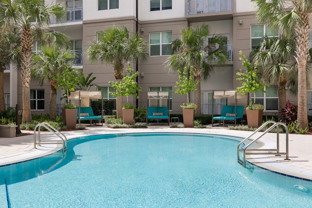 A swimming pool in front of a building surrounded by palm trees.