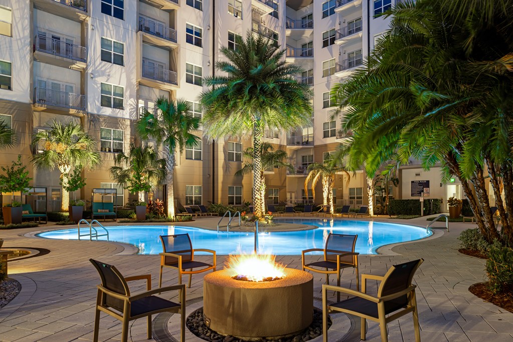 A pool surrounded by chairs and a fire pit in front of a building.