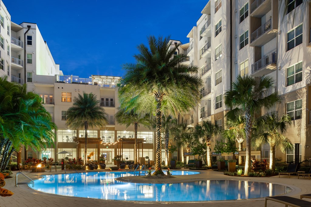 A swimming pool surrounded by palm trees and buildings at night.