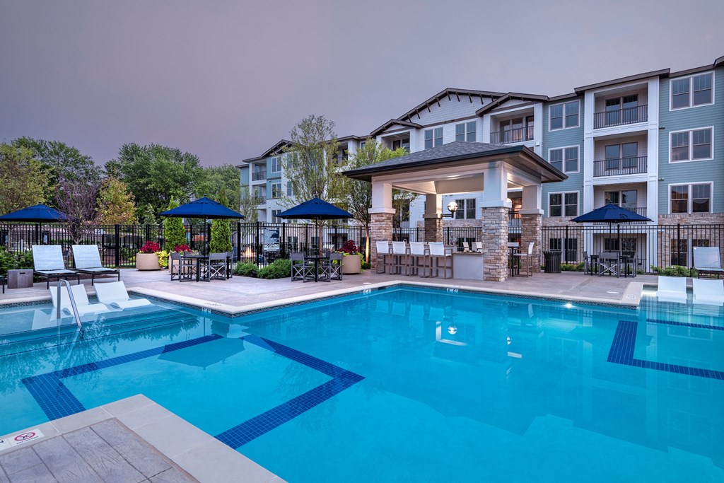 a swimming pool with chairs and umbrellas in front of an apartment building