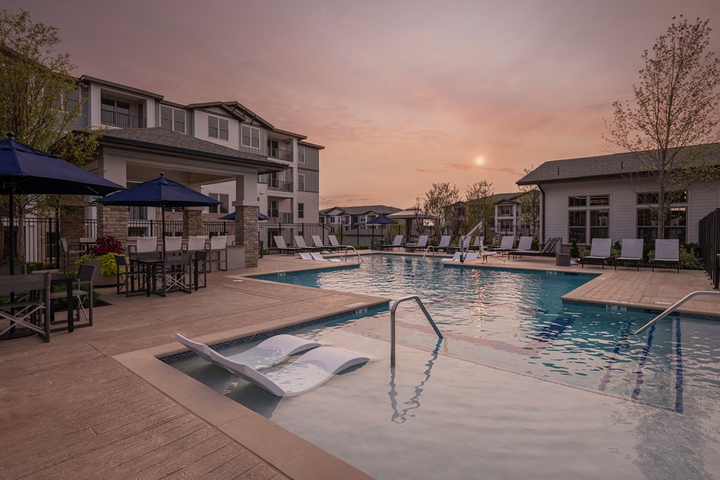 a swimming pool with chairs and umbrellas at sunset