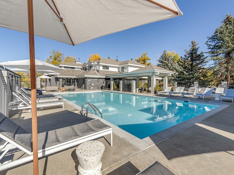 a swimming pool with chairs and umbrellas in front of a house