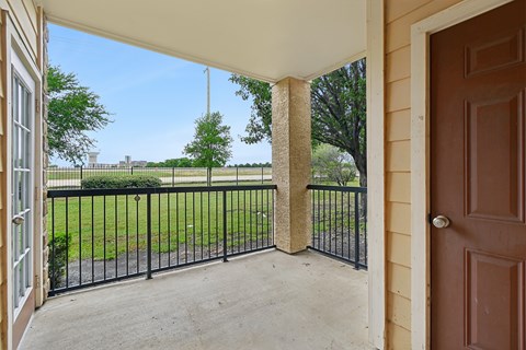 A view from a patio looking out to a green lawn and trees.