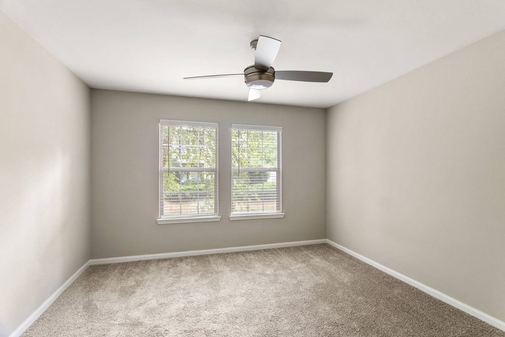 an empty room with two windows and a ceiling fan