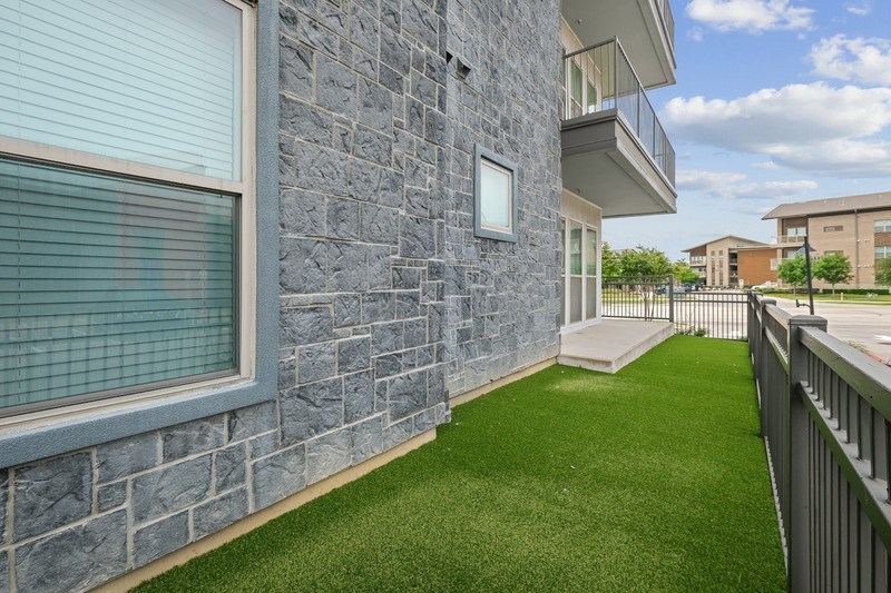 A balcony with a green lawn and a grey stone building.