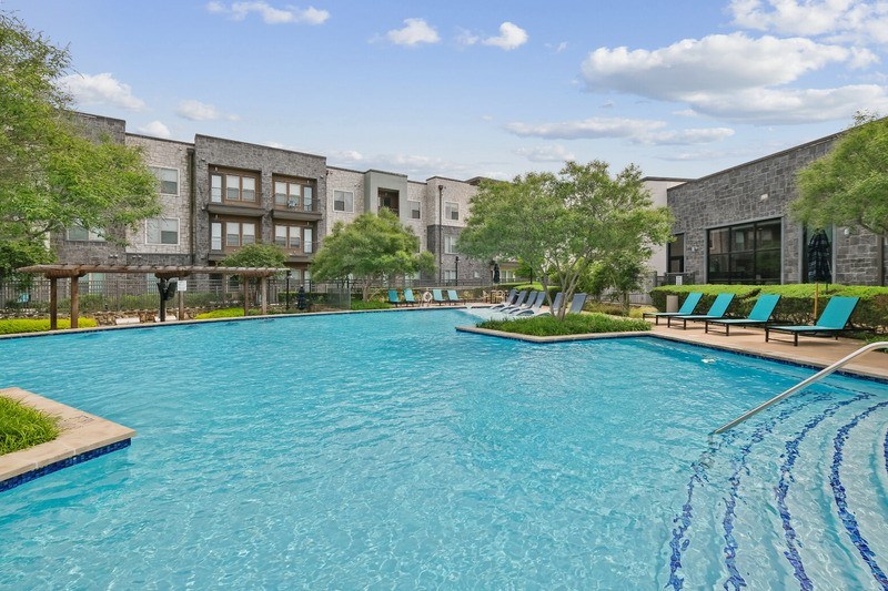 A large swimming pool in front of a building with a fence and trees.