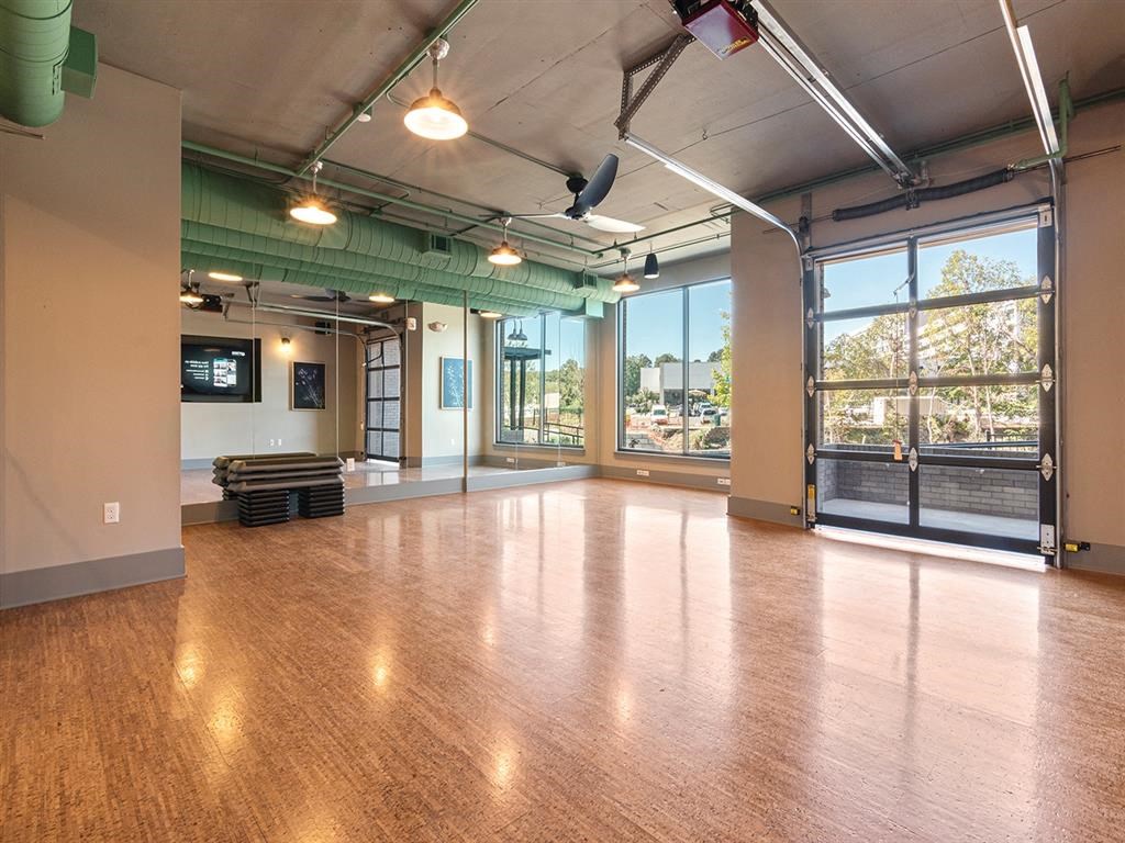A spacious room with wooden floors and a large window overlooking a parking lot.