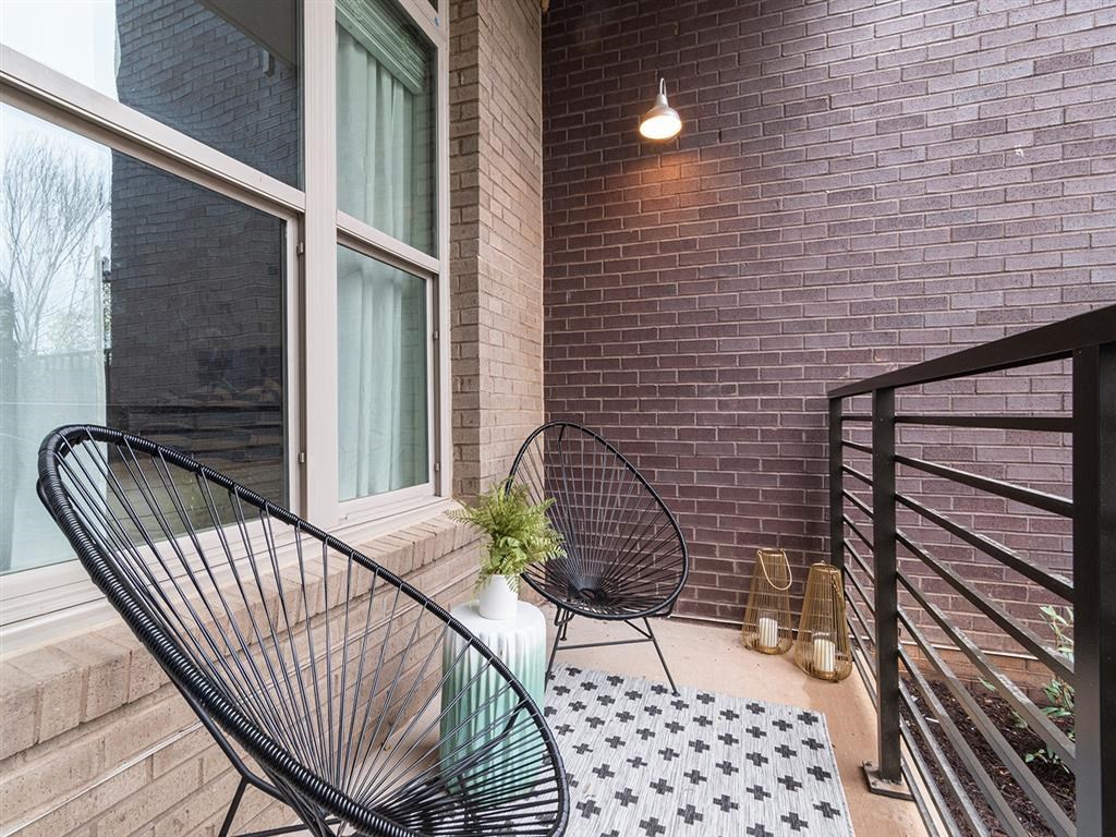 A black metal chair is on a balcony with a table and a vase with a plant.