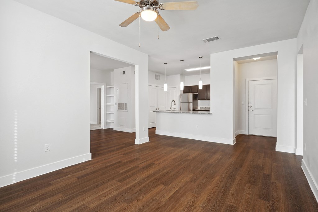 an empty living room with a ceiling fan and a kitchen
