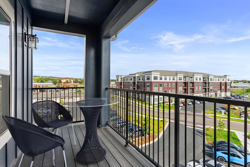 A balcony with a table and chairs overlooking a parking lot and buildings.