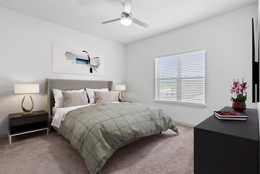 A bedroom with a bed, two lamps, a ceiling fan, and a painting on the wall.