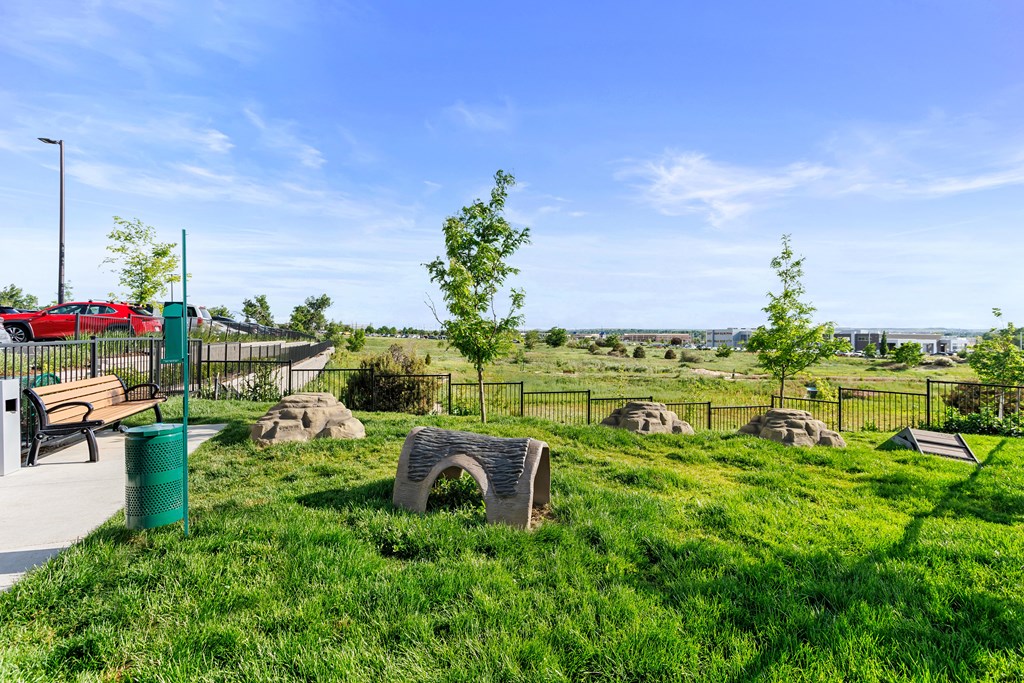 A park with a bench, a trash can, and a fence.