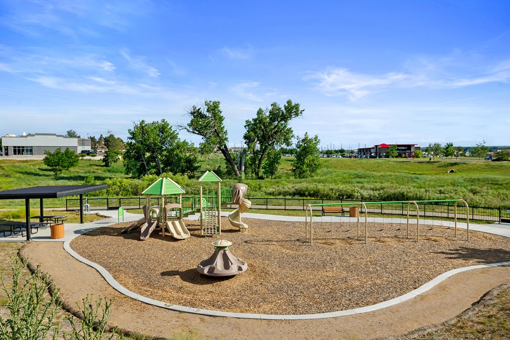 A playground with a green and brown play structure and a white fence.