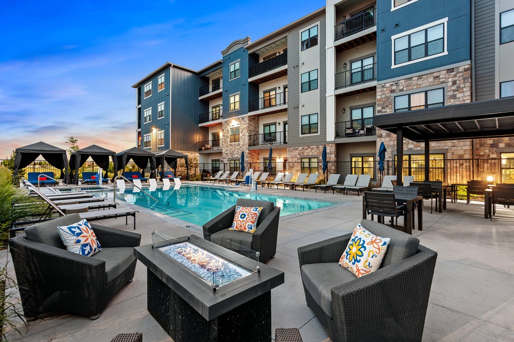 A poolside area with lounge chairs and umbrellas in front of a multi-story building.