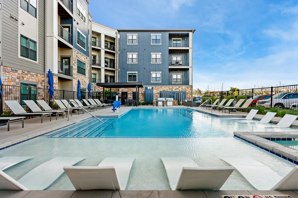 A large swimming pool with lounge chairs and umbrellas in front of a multi-story apartment building.
