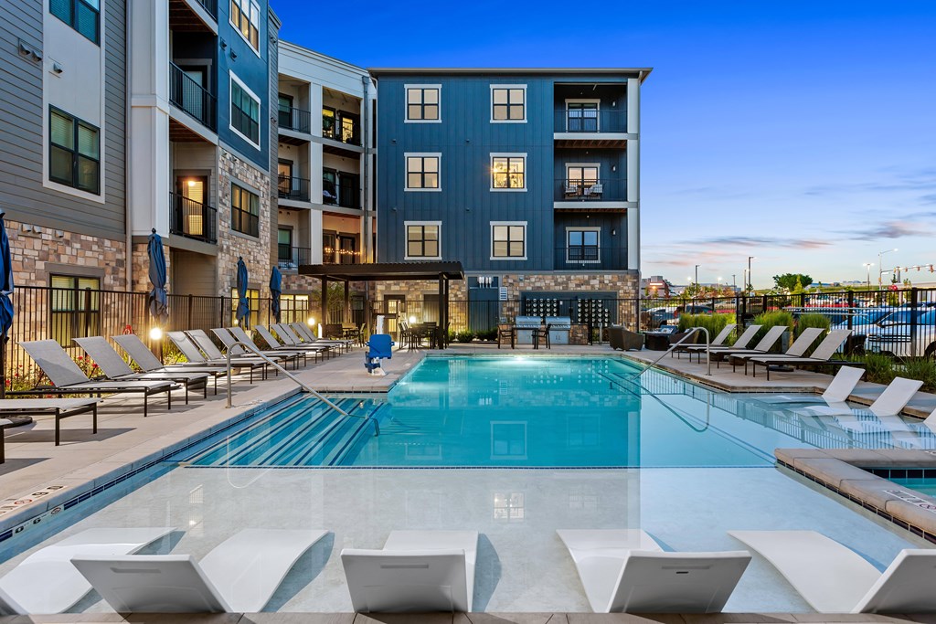 A swimming pool surrounded by lounge chairs in front of a building.
