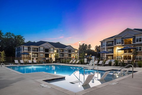 A swimming pool surrounded by lounge chairs in front of apartment buildings.