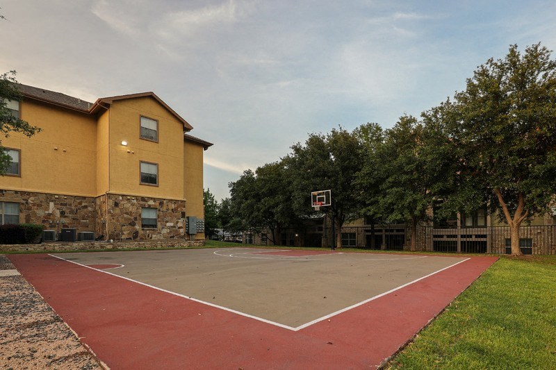 a basketball court in front of a yellow building with trees