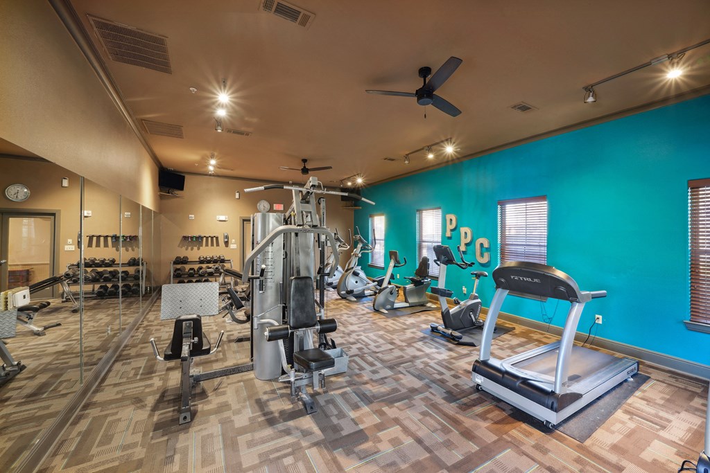 a gym with weights and cardio equipment and a blue wall