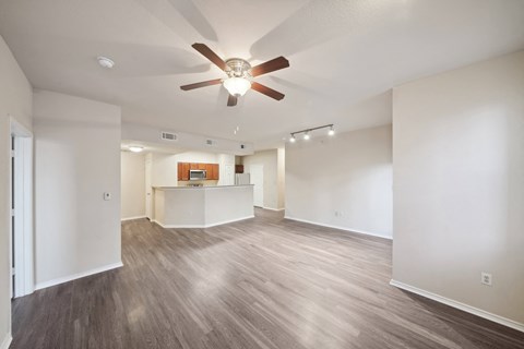 an empty living room with a ceiling fan and a kitchen
