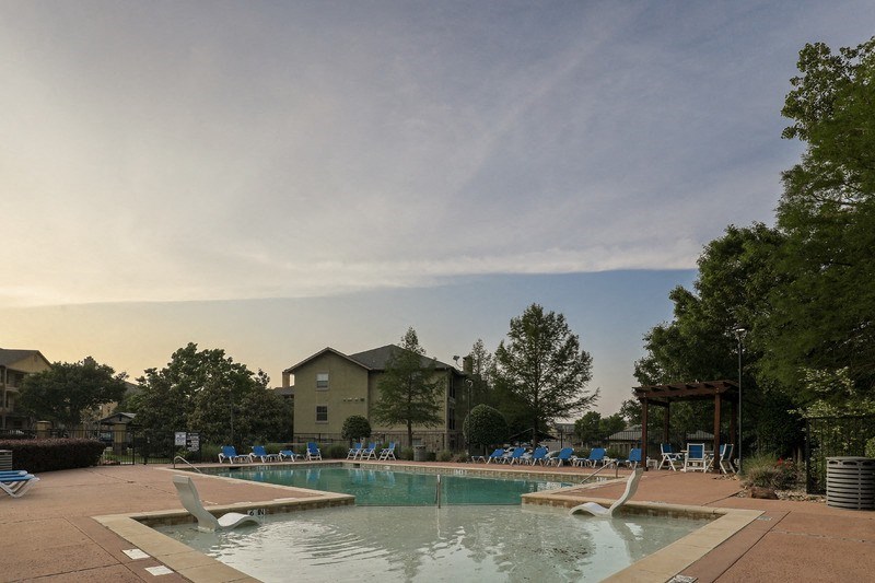 a pool with chairs around it and a house in the background