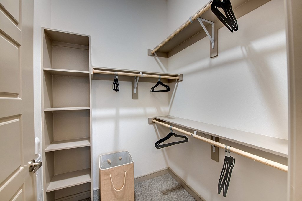 a walk in closet with shelves and hooks and a trash can