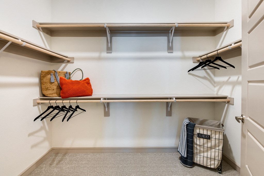 a walk in closet with a white wall and shelves with hangers and a basket