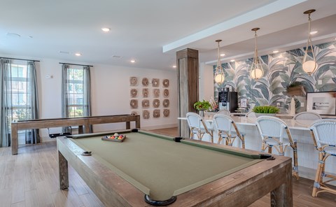A pool table is in the middle of a room with a bar and chairs.