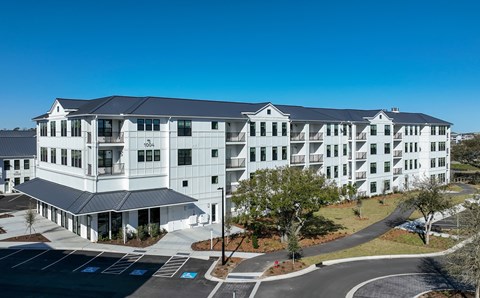 A large white building with a black roof and a parking lot in front.