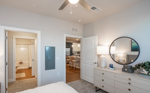 A bedroom with a white dresser and a round mirror on top.
