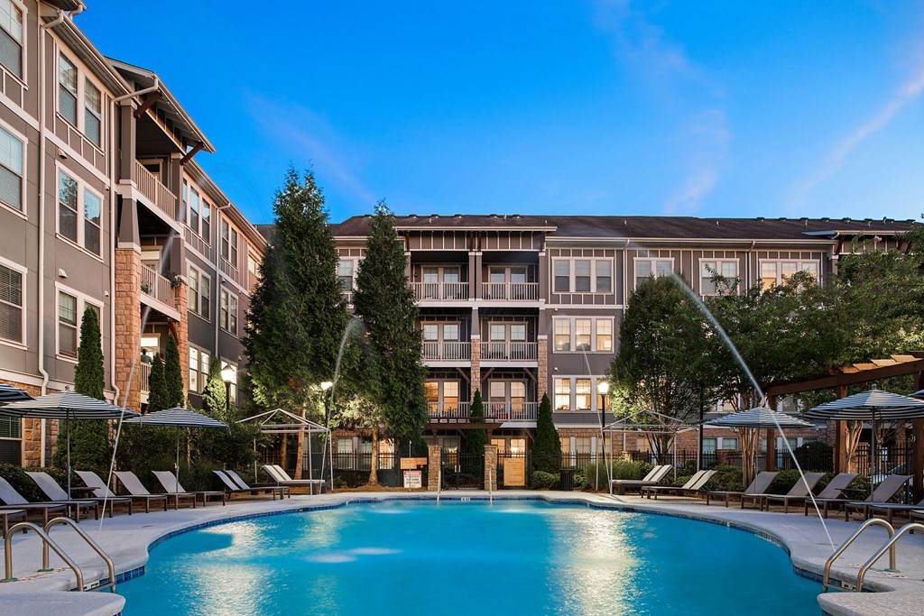 A large swimming pool in front of a building with lounge chairs and umbrellas.