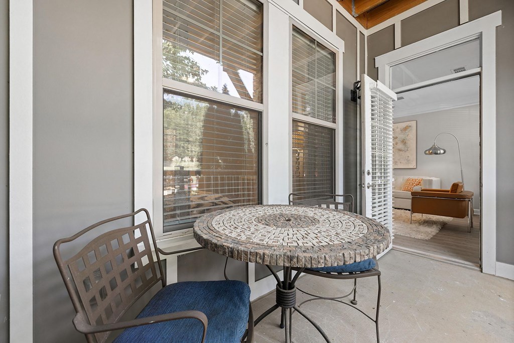A table with a mosaic top is surrounded by chairs in a room with a window.