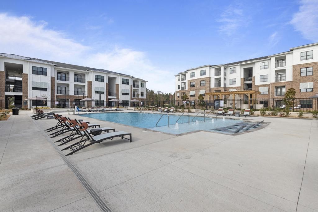 a swimming pool with chaise lounge chairs in front of an apartment building