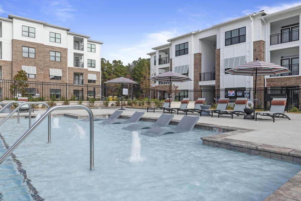 a pool with chairs and umbrellas in front of an apartment building