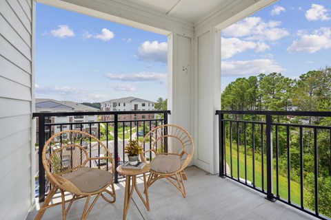 Two chairs are on a balcony with a view of a green lawn and buildings.