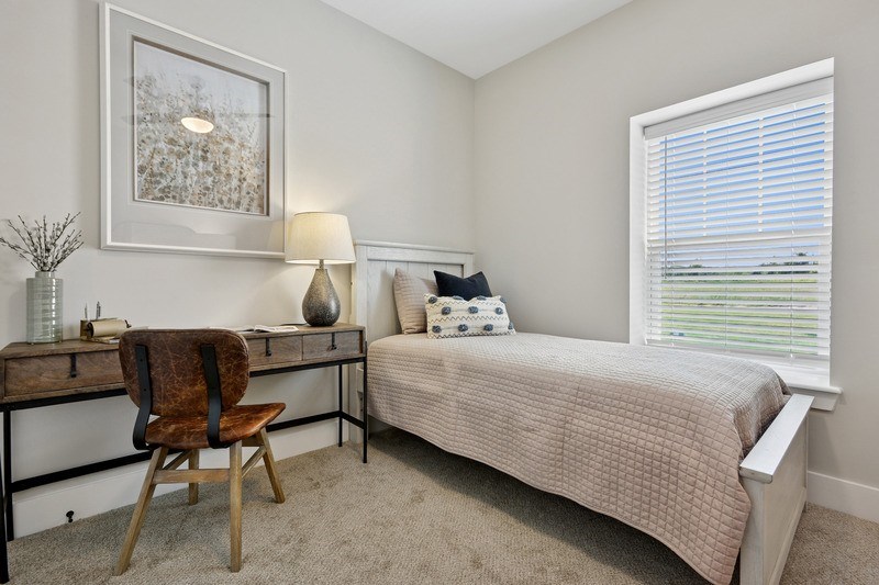 A bedroom with a bed, desk, chair, and window.