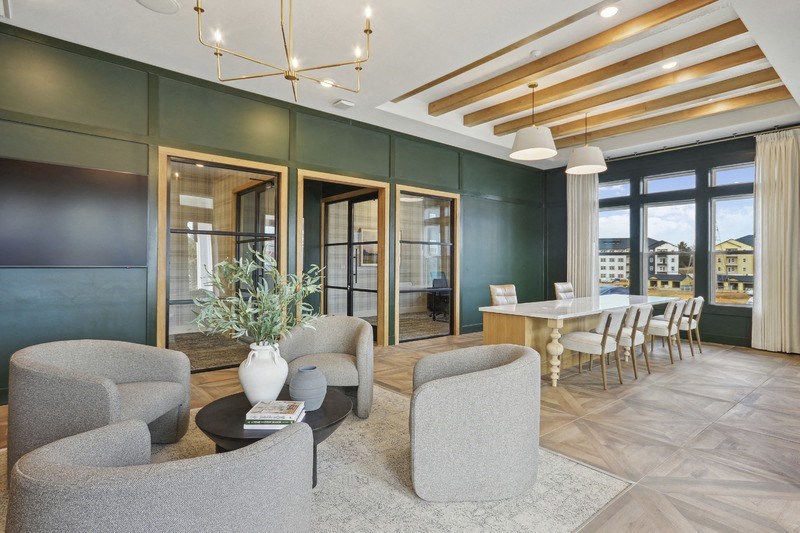 A living room with a grey sofa, a grey armchair, a white vase with a plant, a black coffee table, and a wooden floor.